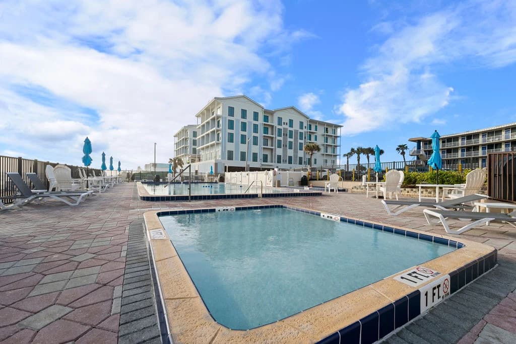Rooftop pool area with lounge chairs and ocean view, beneath a blue sky.