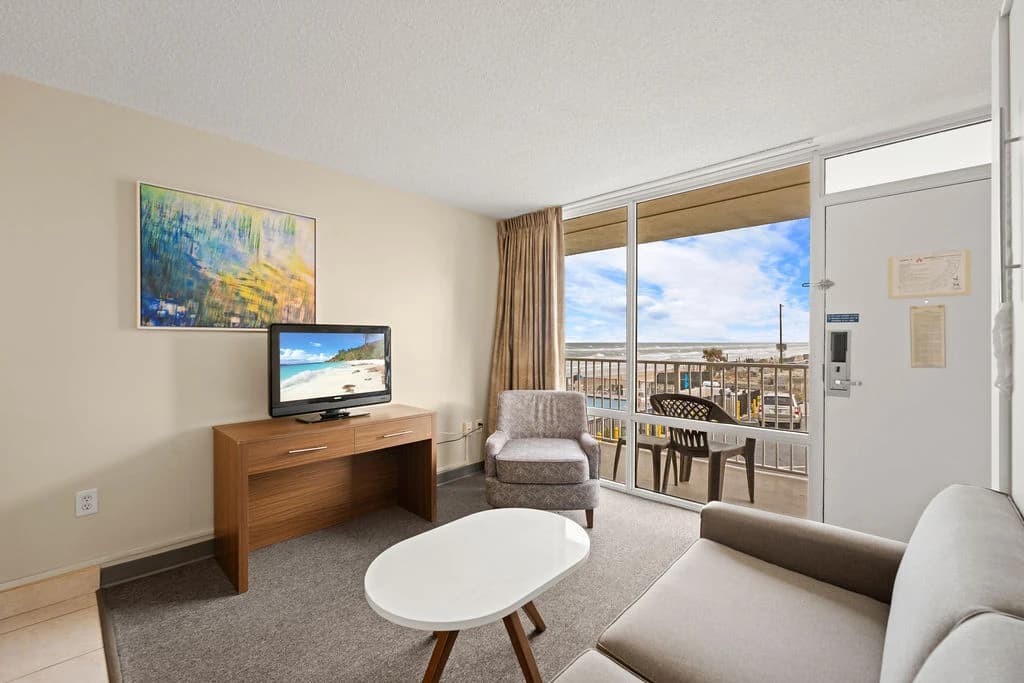Cozy living area with sofa, TV, balcony access, and ocean view.